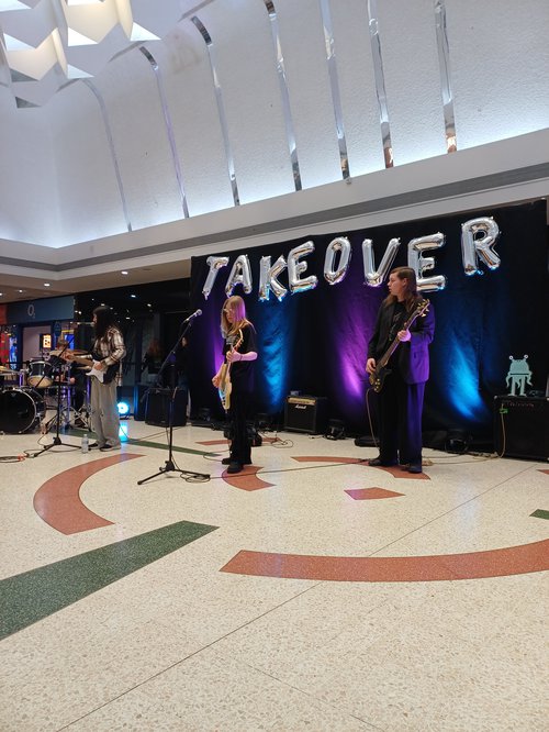 A band with 3 members all playing guitar in a shopping centre.