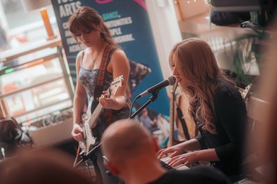2 female performers, one playing guitar and one singing and playing keyboard