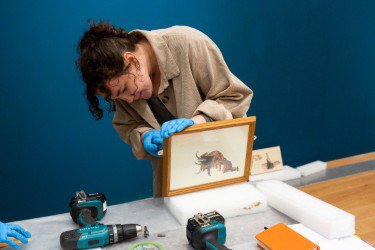 Photo of maker Bailey Revill, working on a wooden frame, with tools laid out around her.