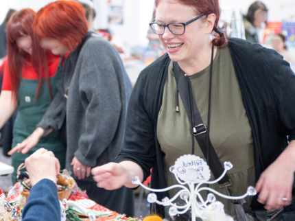 Woman in a khaki green dress with red hair buying something from a stall at a market