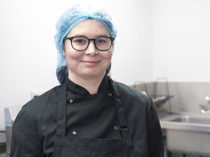 An Inspire College student in a chef uniform and hairnet, holding a tray of bacon.