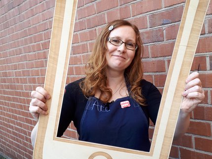 Photo of maker Clare Taylor holding up a wooden frame, designed to look like a phone or tablet
