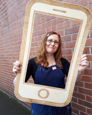 Photo of maker Clare Taylor holding up a wooden frame, designed to look like a phone or tablet
