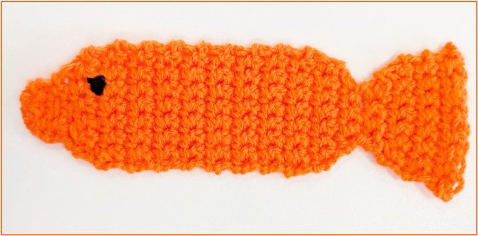 An orange crocheted bookmark, shaped like a fish