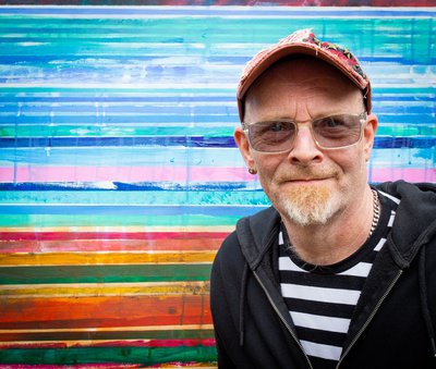 portrait of a man in a cap smiling in front of a multicoloured backdrop