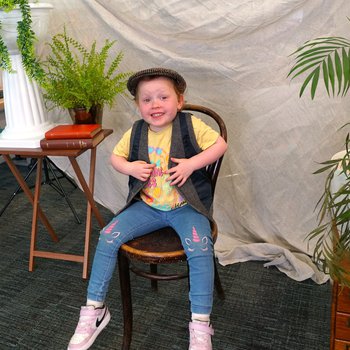 A little girl dressed in an Edwardian hat and waistcoat posing for a picture.