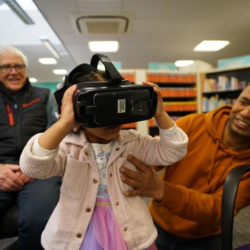 A photo of a little girl using the VR headset with her dad.
