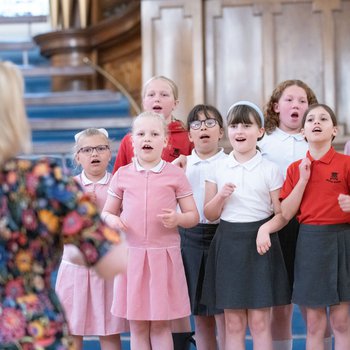 A teacher wearing a floral dress leads a chorus of young singers