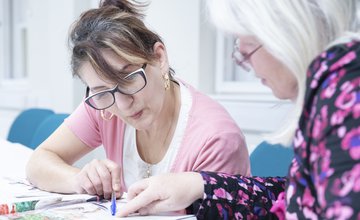 A woman wearing pink looking at written text with a tutor.