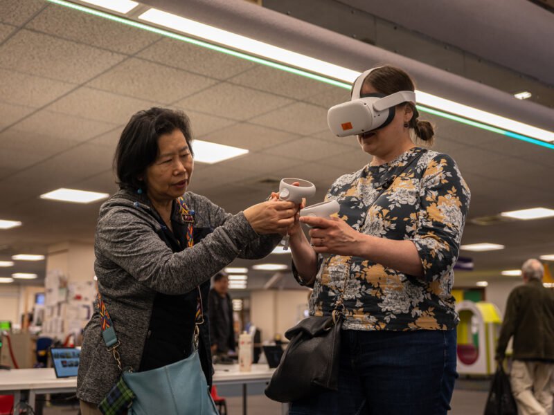 Someone helping another person to hold the controls of a VR headset