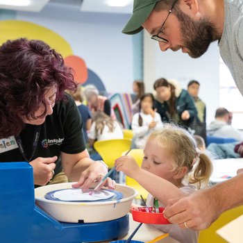 young girl using a paint wheel with help from her dad and an Inspire member of staff
