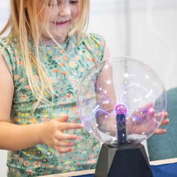 A girl placing her hands on the edges of a giant plasma ball.