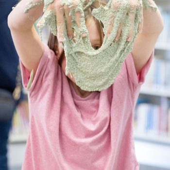 A girl holding up slime in front of her face.