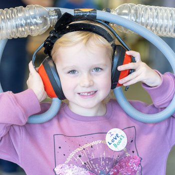 A girl wearing hand-made headphones and tubes as part of a science trick.