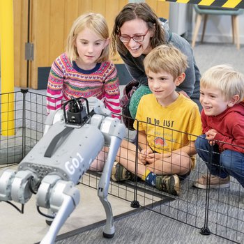 A woman and three young children looking at a robot dog.