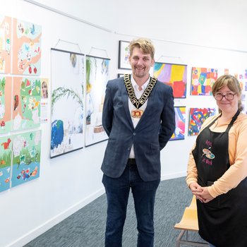 A councillor and artist standing together in front of an art exhibition.