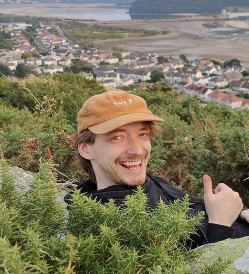 A photo of Harry Lenton wearing an orange cap, smiling and doing thumbs up