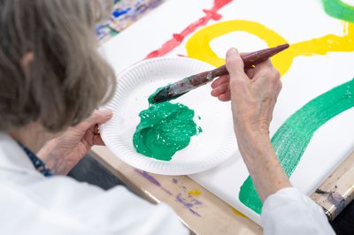 An elderly person is painting with bright green paint.