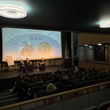 Stage with two authors sat with an interviewer and Q&A in text at the  back