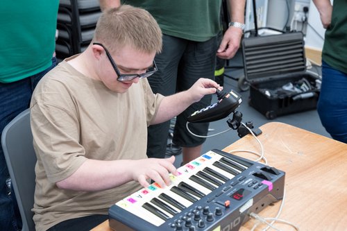 A man smiling playing a keyboard and CMPSR instrument