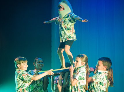 Five young dancers lifting a dancer wearing a shark hat
