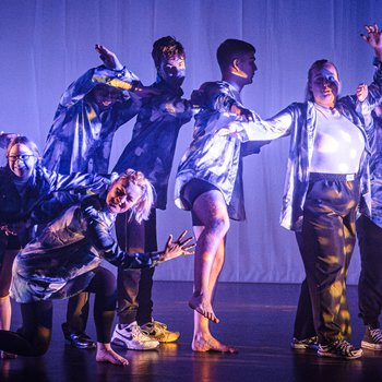 Nine dancers performing on stage with blue lighting