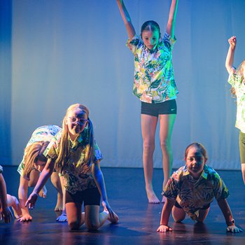 Dancers in surf shirts, two standing with arms in the air and 4 crouching down