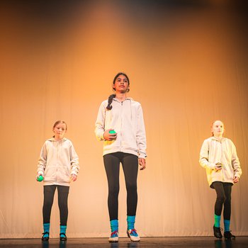 Three dancers in grey hoodies and black tap shoes standing center stage