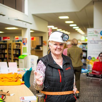 A stallholder from Nottinghamshire Mining Museum wearing a miner's helmet with lamp and holding up a miner's lamp.