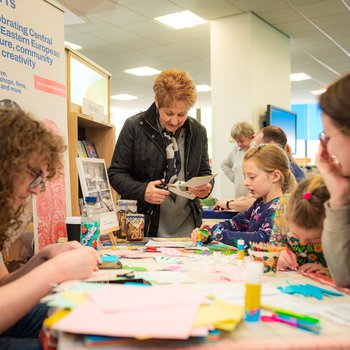 Stallholders from CEE Notts helping 2 girls and a woman do a craft activity.