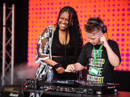 A black woman smiling, and a young boy DJing on stage