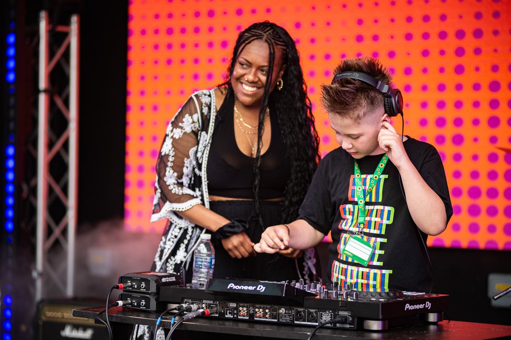 A black woman smiling, and a young boy DJing on stage