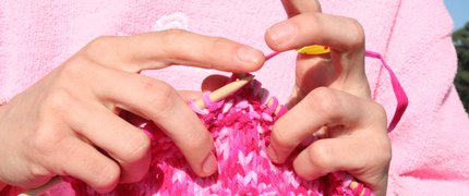 hands knitting a pink and white scarf
