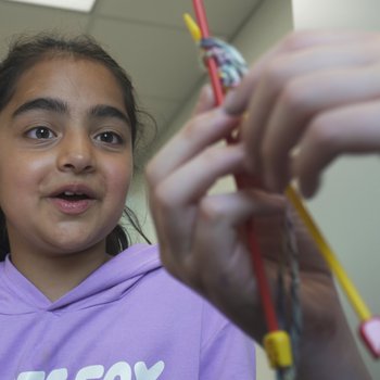 A girl watches someone knit with interest