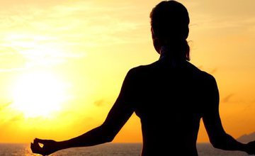 A woman sits and meditates in front of a sunset