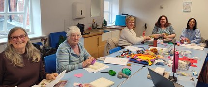 A group of older ladies are sat round a table working on craft projects.
