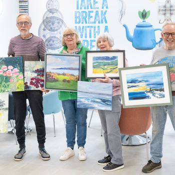Group of learners from a painting course stood smiling holding their work