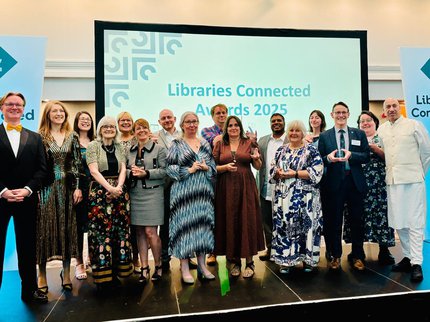 A group of people with Peter Gaw centre right, on the stage holding their awards at the libraries connected awards