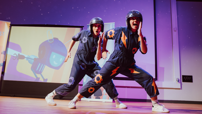 Two actors playing robots in The Greatest Robot Ever, dancing in front of a screen