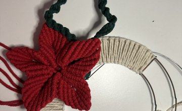 Metal ring partly covered with cream macrame loops and a red macrame Christmas flower with an outline of a holy leaf