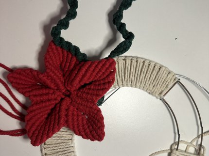 Metal ring partly covered with cream macrame loops and a red macrame Christmas flower with an outline of a holy leaf