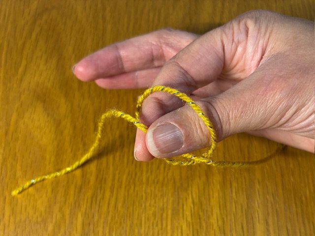 Photo of fingers reaching through a loop in a piece of yarn and grabbing the trailing tail