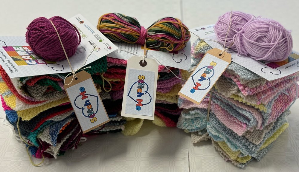Three piles of knitted squares, labelled 'Stitch Me'