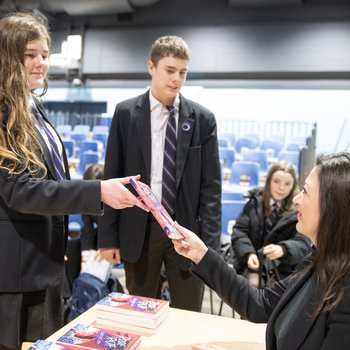 Author Sufiya Ahmed wears a black suit and signs copies of her book for a group of school children