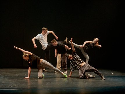Five young dancers dressed in black and white performing on stage with their legs outstretched.