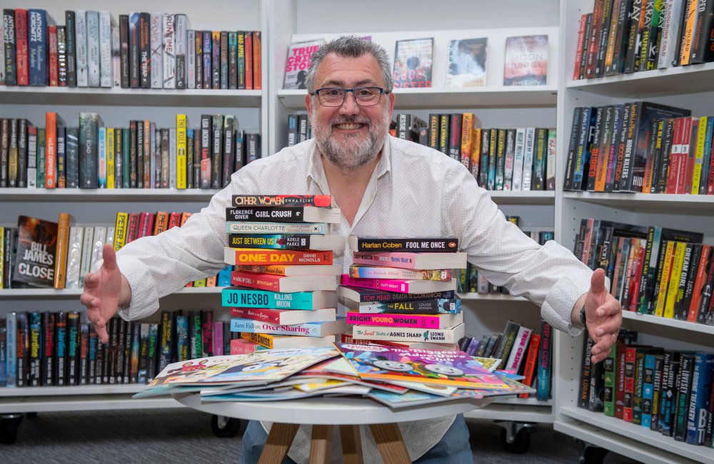 Worksop library manager smiling and posing with a stack of books donated to them