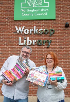 Worksop staff members smile with books in front of Worksop Library
