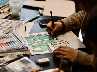Hands drawing surrounded by art materials