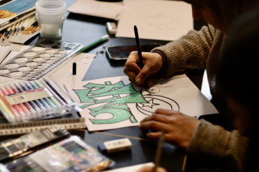 Hands drawing surrounded by art materials