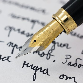 Image of a pen on paper with handwriting in the background